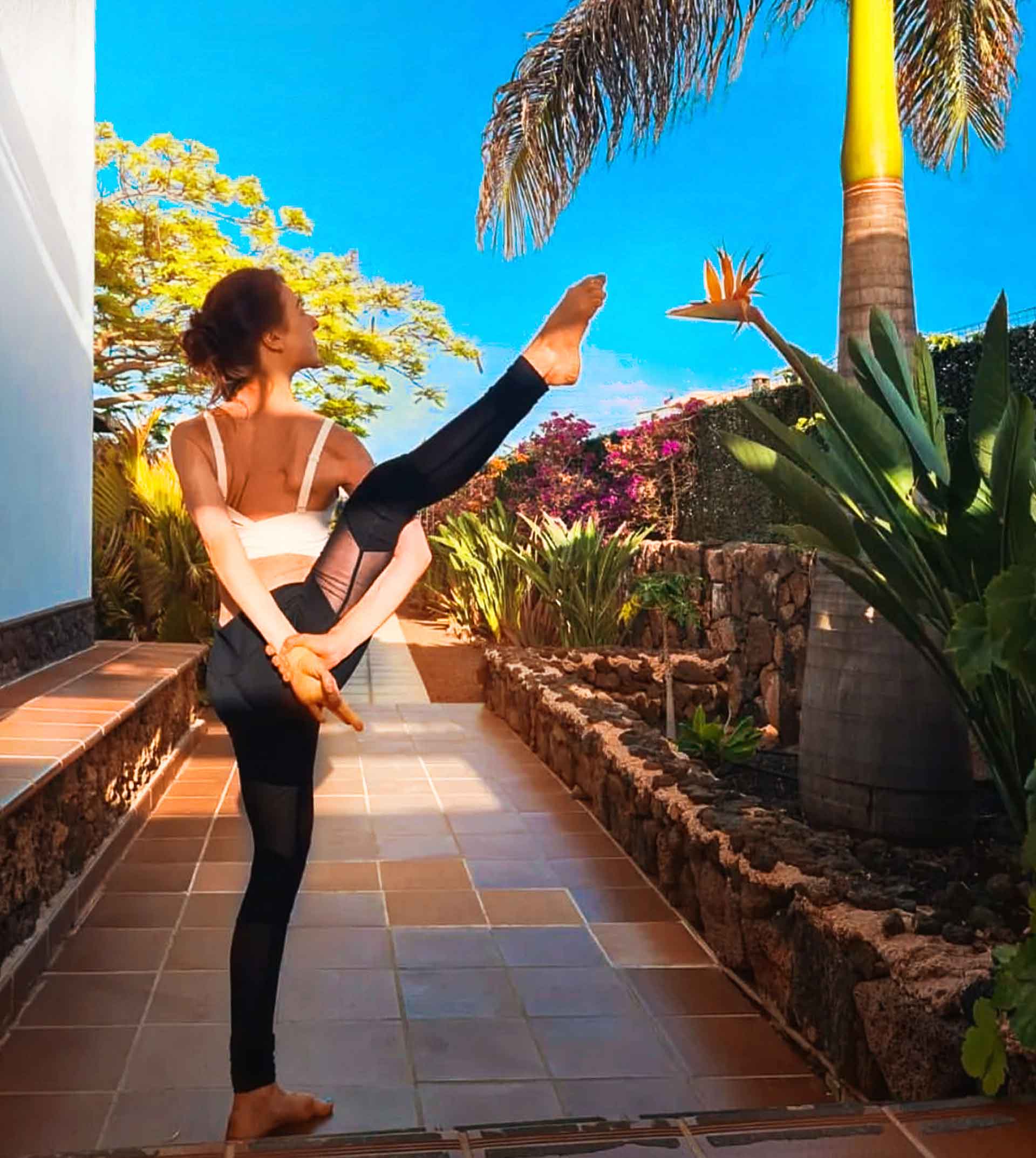 Young woman practising Bird of Paradise yoga pose beside a Bird of Paradise flower at Villa Azul