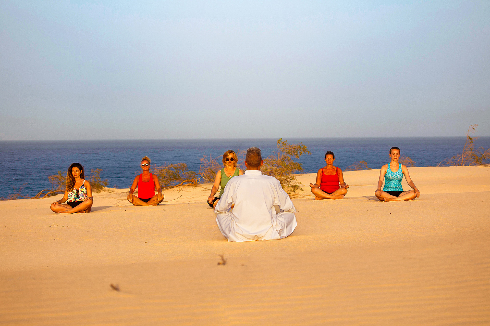 Qigong teacher leading a meditation class in the Corralejo dunes overlooking the sea, Fuerteventura