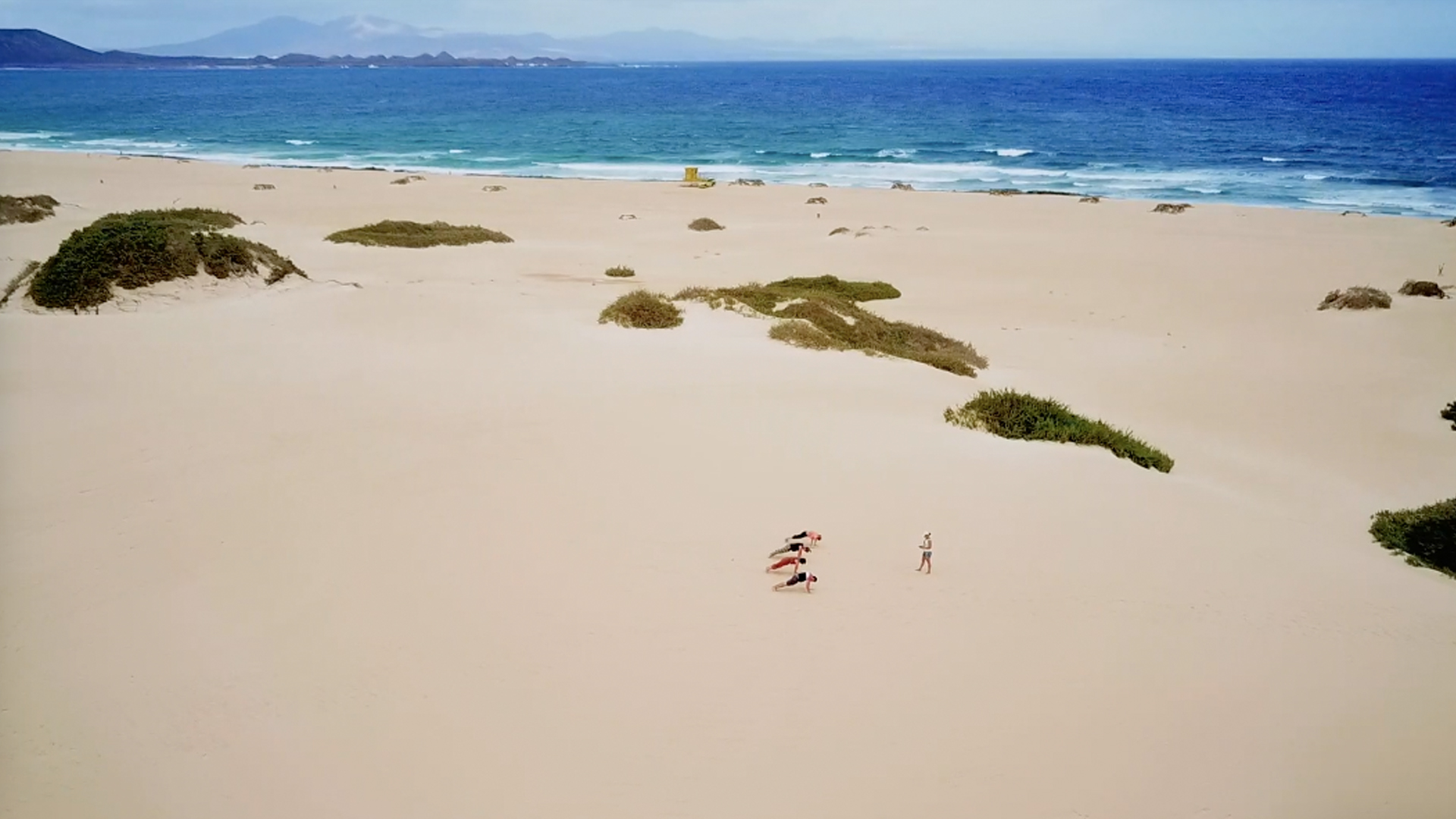 Small group practising Kumbhakasana in the Corralejo dunes with the sea in the background