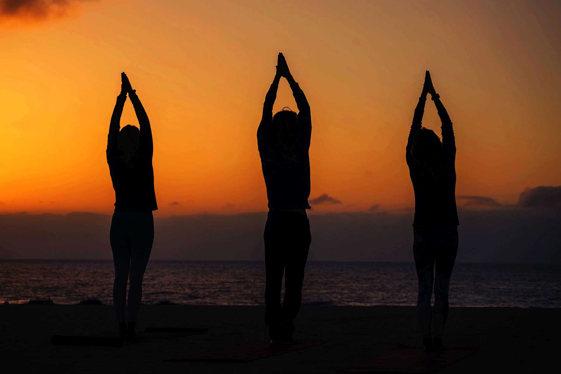 Three women practicing yoga at sunrise on a beach in Fuerteventura